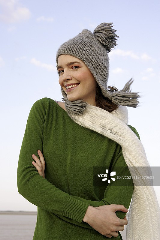 穿着绿色毛衣、牛仔裤和围巾，双手交叉微笑的美丽女人图片素材