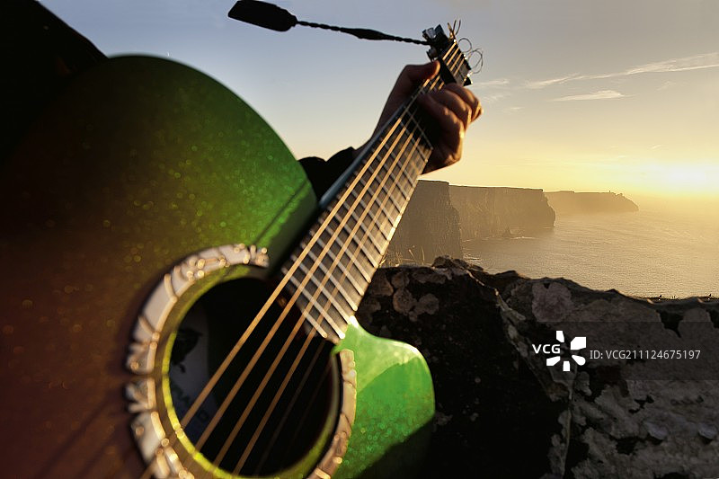 在爱尔兰莫赫悬崖日落时分弹吉他的男人特写图片素材
