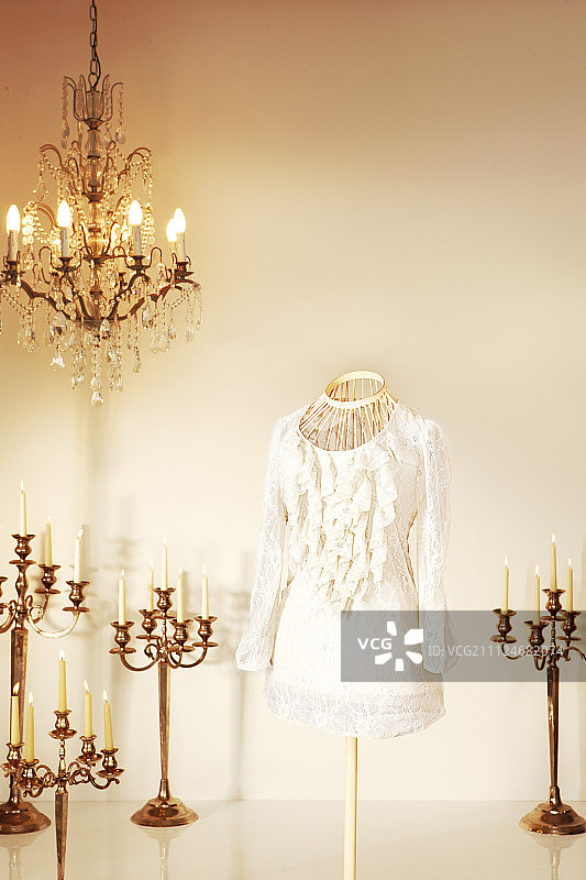 人体模型上的白色褶皱女式衬衫，周围环绕着枝形吊灯和烛台图片素材