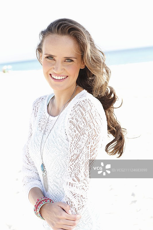 一位在海滩上身穿白色蕾丝连衣裙的年轻长发女子图片素材