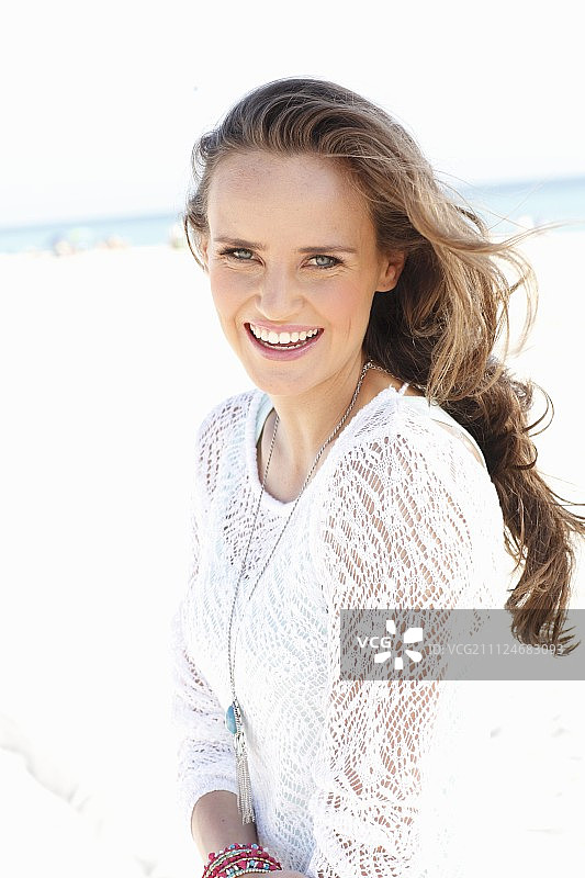 在海滩上穿着白色蕾丝连衣裙的年轻长发女人图片素材