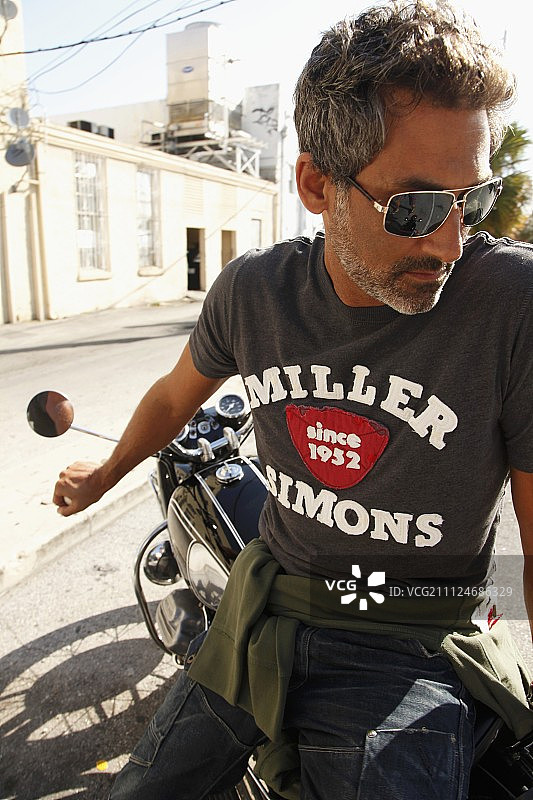 男人戴着太阳镜，穿着牛仔裤和T恤，坐在摩托车上图片素材