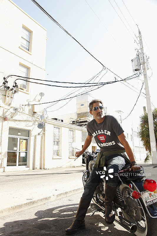 男人戴着太阳镜，穿着牛仔裤和T恤，坐在摩托车上图片素材