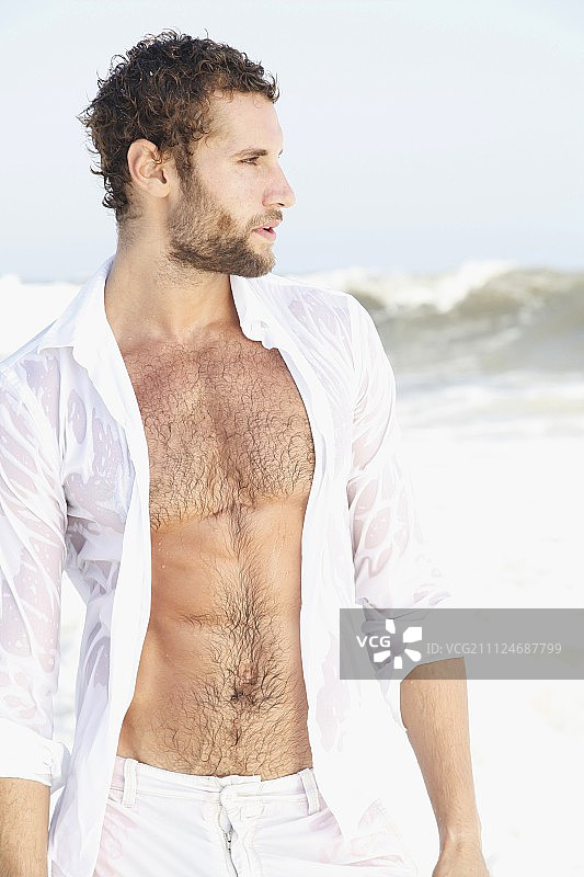 穿着白色湿衬衫和百慕大短裤的年轻男人站在海边图片素材