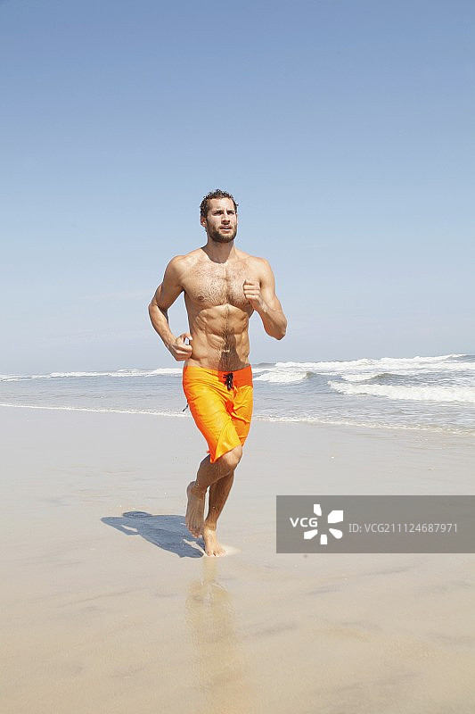 穿着黄色百慕大短裤的健壮年轻人沿着海滩慢跑图片素材