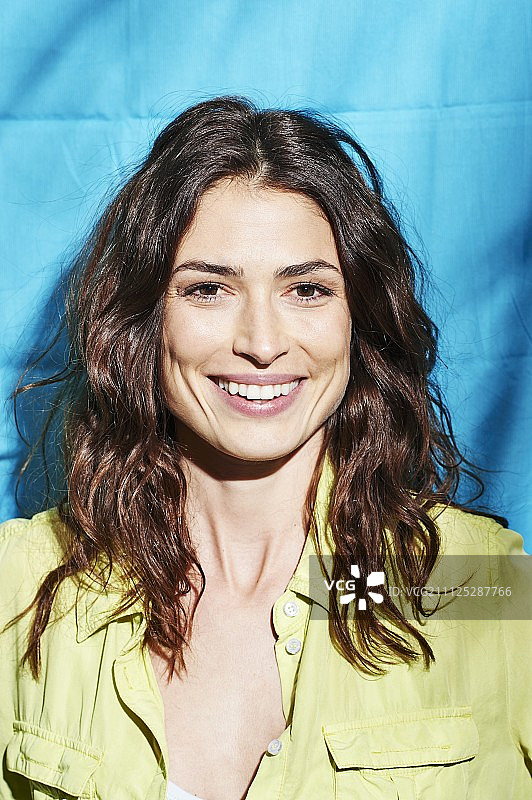 蓝色背景下，穿着黄色衬衫的棕发女子图片素材