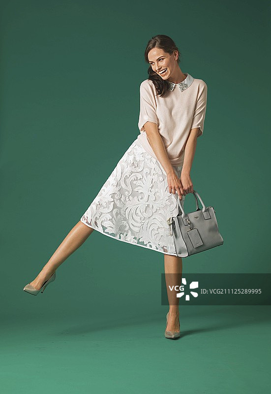 一位身穿及膝蕾丝裙、饰有水钻的针织套头衫和浅口鞋的棕发女子图片素材