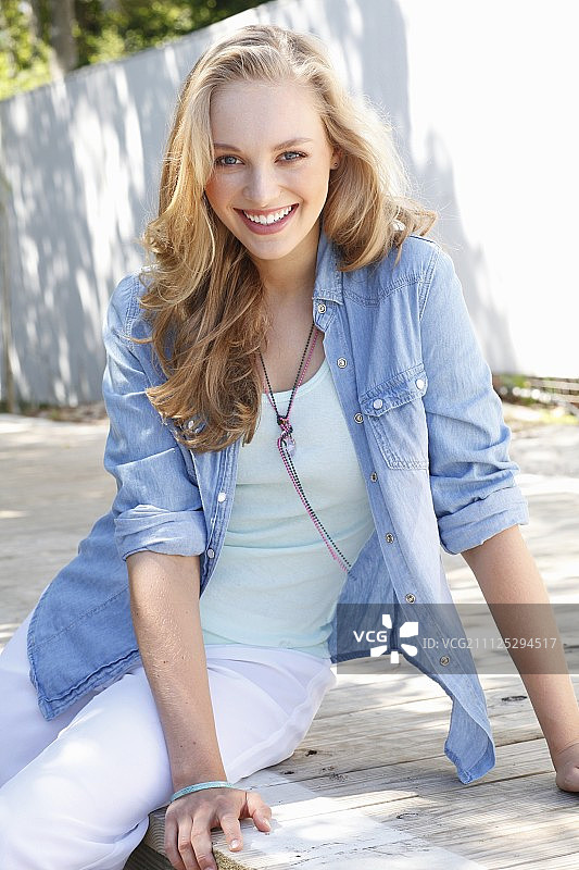 一位穿着浅色上衣、白色长裤和牛仔衬衫的年轻金发女子图片素材