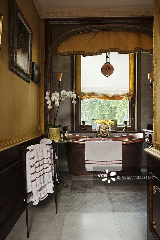 格鲁吉亚风格的黄色浴室，窗户下设有独立铜浴缸，配有檐板和罗马帘图片素材
