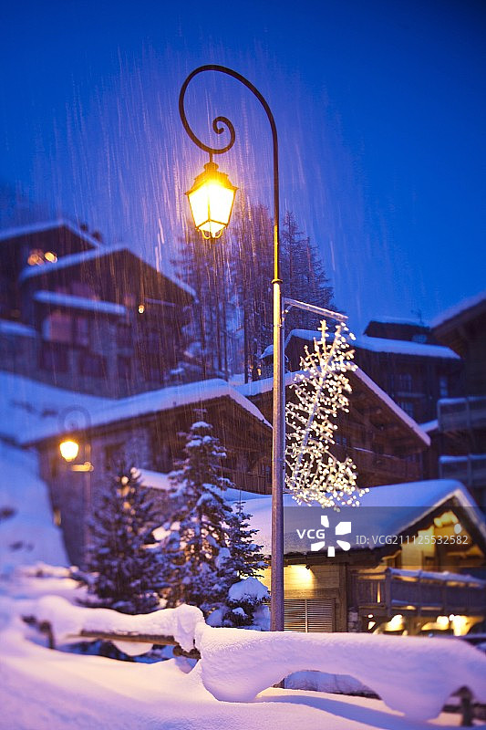 黄昏时分斜坡上木屋中的照明窗户，前景中有照明路灯图片素材