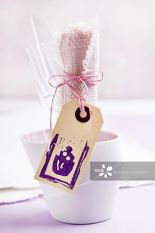 烧杯中的塑料餐具和粉色亚麻餐巾；带有橡胶印蛋糕的木制标签图片素材