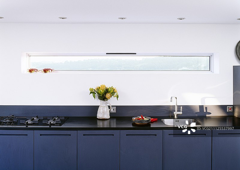设计师设计的长厨房台面，蓝色底座单元靠墙，配有狭窄的带状窗户图片素材
