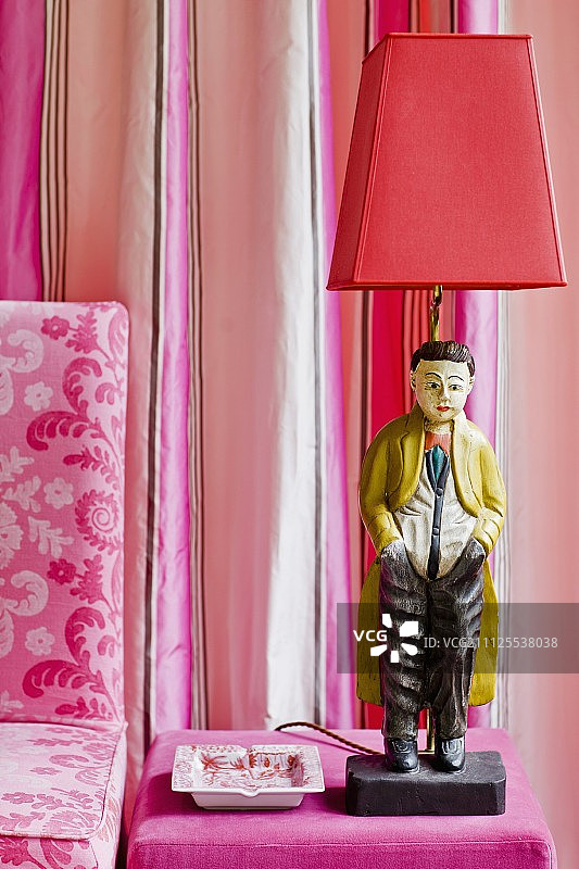 粉色天鹅绒脚凳上的中式雕像台灯，搭配条纹真丝塔夫绸窗帘和印花亚麻椅子装饰图片素材