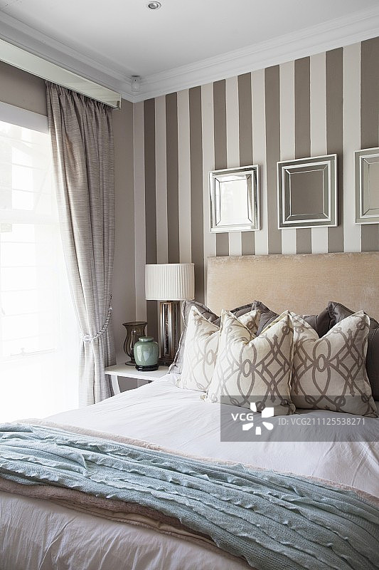 双人床后，优雅条纹壁纸上的镜框图片素材