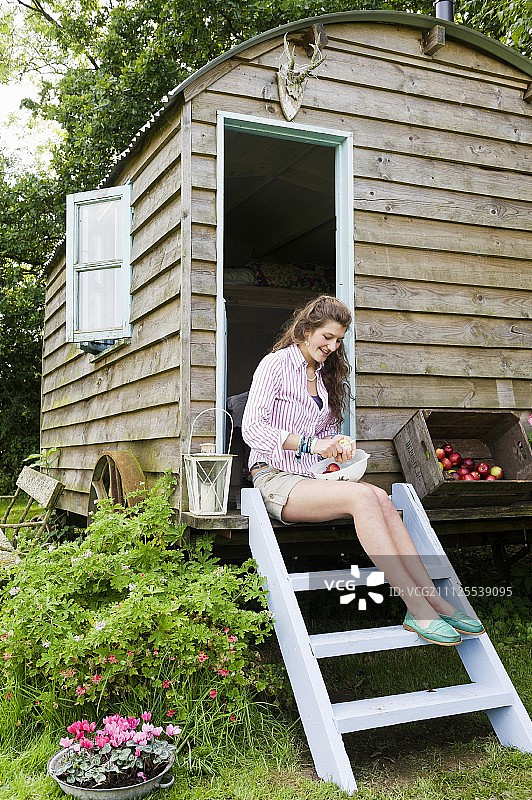 女人坐在通往绿色怀旧牧羊人小屋的淡蓝色梯子旁的苹果箱旁边图片素材