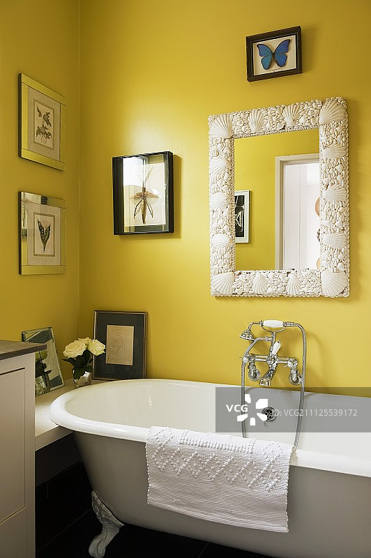 昆虫图案和贝壳马赛克镜子装饰的黄色墙壁旁的怀旧浴缸图片素材