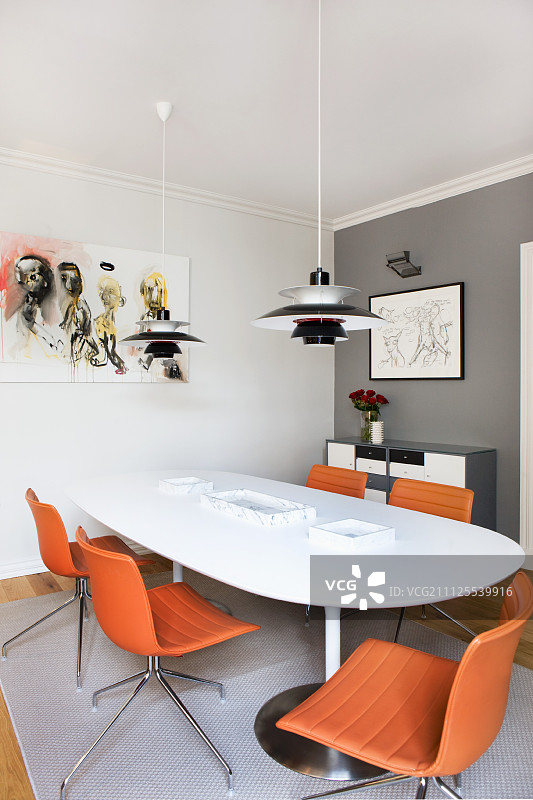 白色餐桌和转椅上的Poulsen吊灯，橙色皮革椅套，灰色墙角图片素材