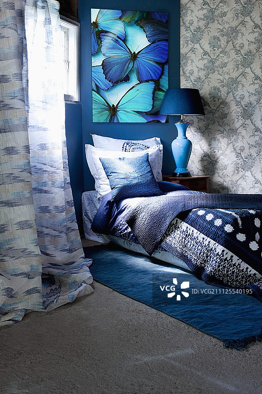 蓝色调毛毯、枕头和靠垫的床，背景是蓝绿色的蝴蝶画图片素材