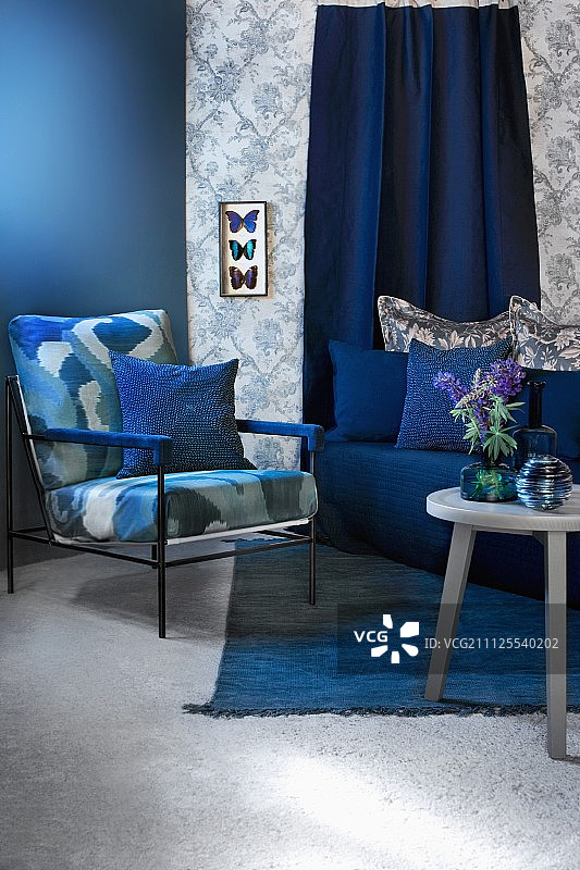 蓝色调的座位区，配有扶手椅、沙发和边桌；图案壁纸上陈列着蝴蝶标本图片素材