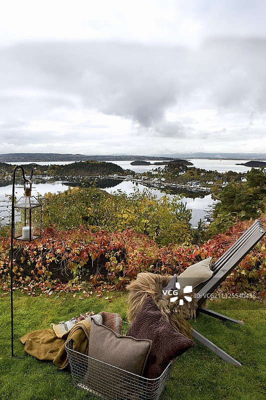 秋季花园中带有毛皮毯、靠垫和灯笼的花园椅，可欣赏挪威礁海岸的景色图片素材