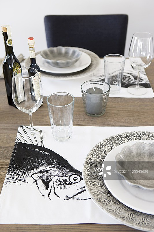 黑色和白色餐垫上带有灰色餐盘的餐桌布置，有鱼图案图片素材
