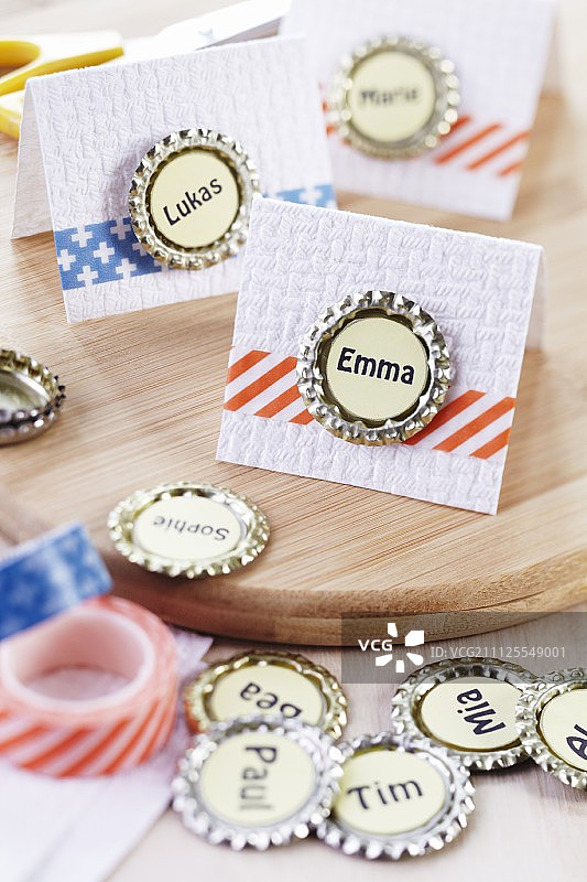 用扁平瓶盖和纸胶带装饰的餐位卡，置于木质表面图片素材