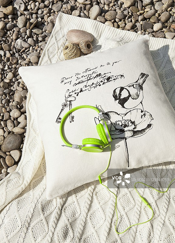 砾石地面上靠垫和羊毛毯上的霓虹绿时尚耳机图片素材
