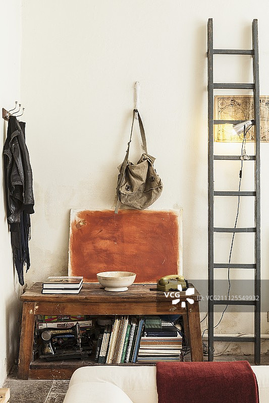 开放式复古木柜中的书籍和古董缝纫机，木梯上的夹灯和衣帽钉之间的彩绘帆布图片素材