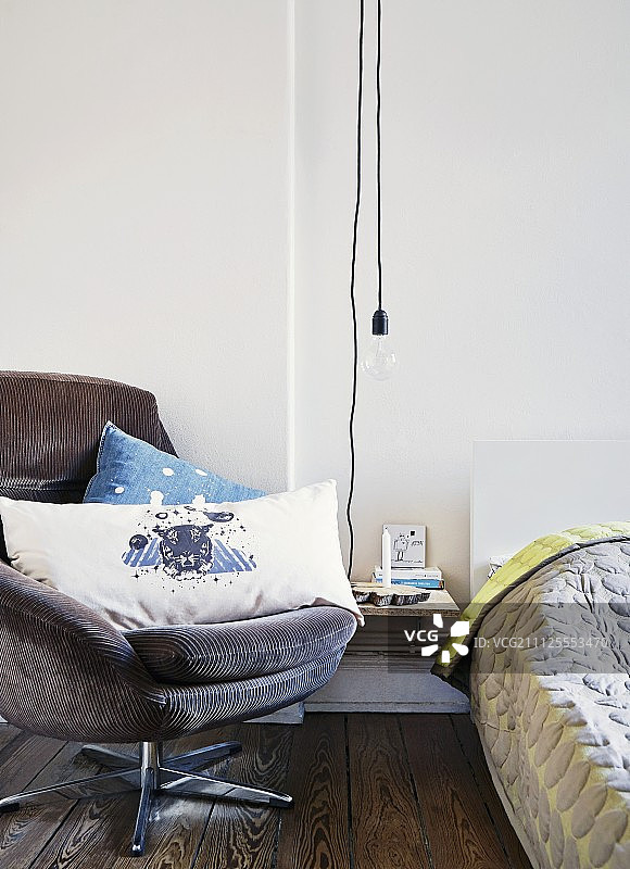 DIY床头柜，床和丹麦设计师床罩之间用简单的灯泡照明，灯芯绒扶手椅上放着老虎图案靠垫图片素材