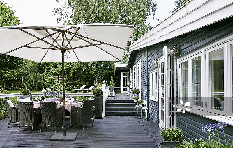 露台上用于户外休闲的现代家具和白色遮阳伞；深色木镶板露台地板和房屋外墙图片素材