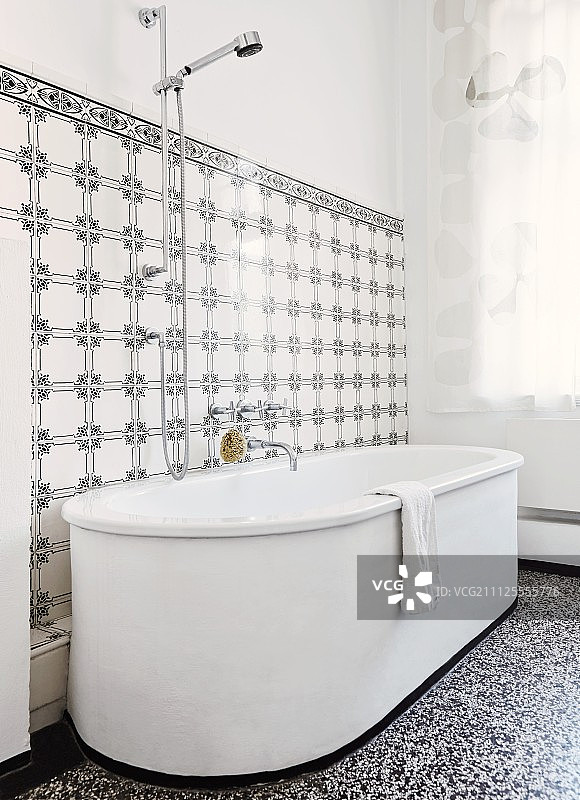水磨石地板上的白色独立浴缸，背景是黑白复古图案瓷砖墙图片素材