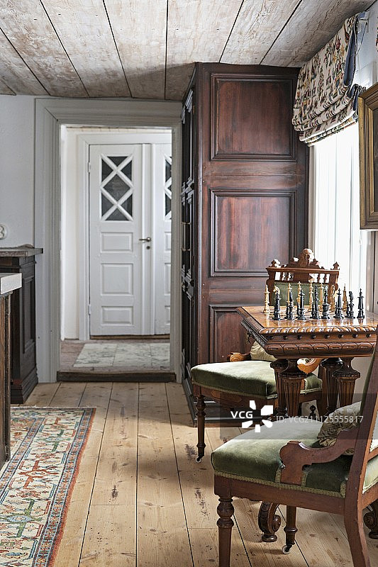 木地板和天花板的乡村室内，窗边的古董软垫椅和棋桌图片素材