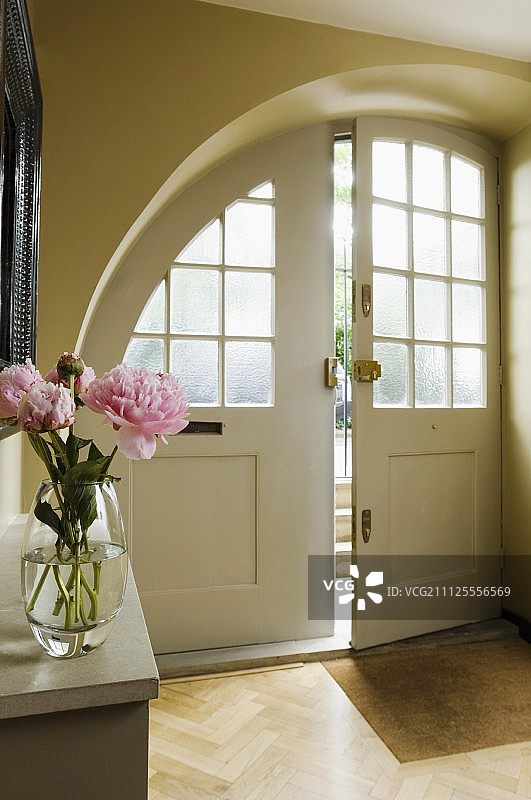 拱形前门，门厅内有格子窗，前景是控制台架子上的花束图片素材