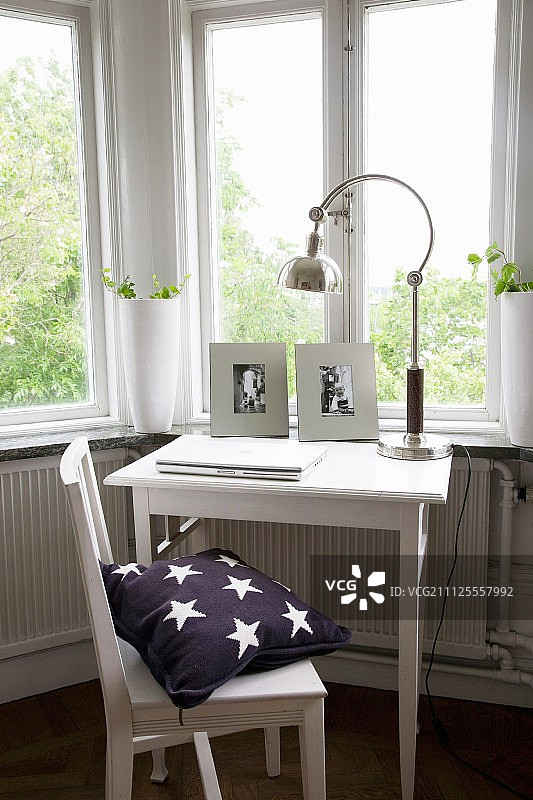 窗户下方的小工作区，配有白色油漆的椅子、桌子和复古台灯图片素材