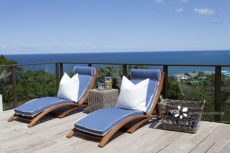 木质露台上带蓝色床垫和白色枕头的日光浴躺椅，可全景欣赏海景图片素材
