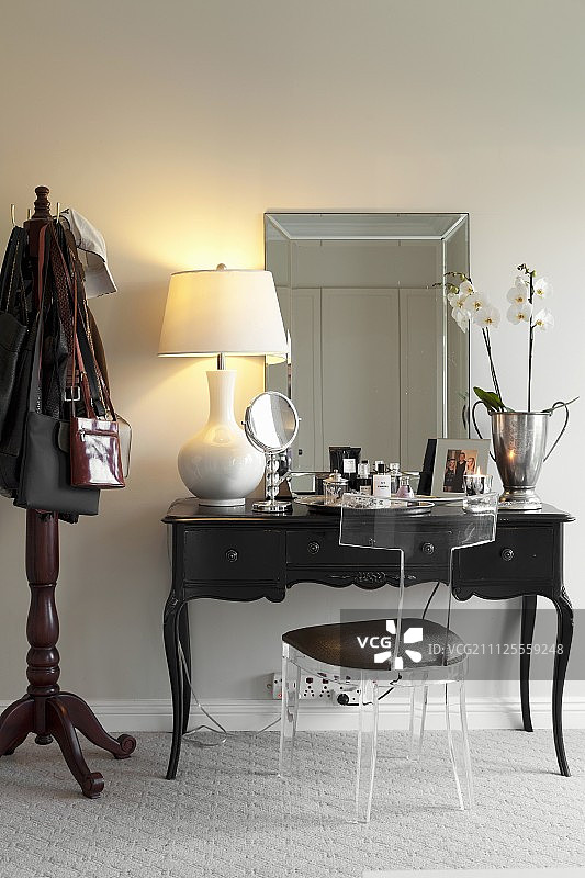 古董深色木梳妆台上的有机玻璃椅子和带淡色灯罩的台灯图片素材