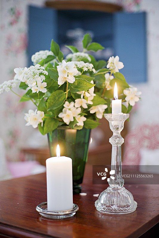 木桌上绿色茉莉花瓶前的玻璃烛台中圆柱蜡烛和标准蜡烛图片素材