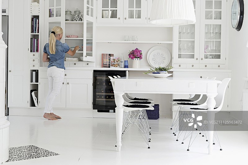 乡村风格餐厅：白色餐桌、经典伊姆斯椅与白色餐具柜，背景中的女人图片素材