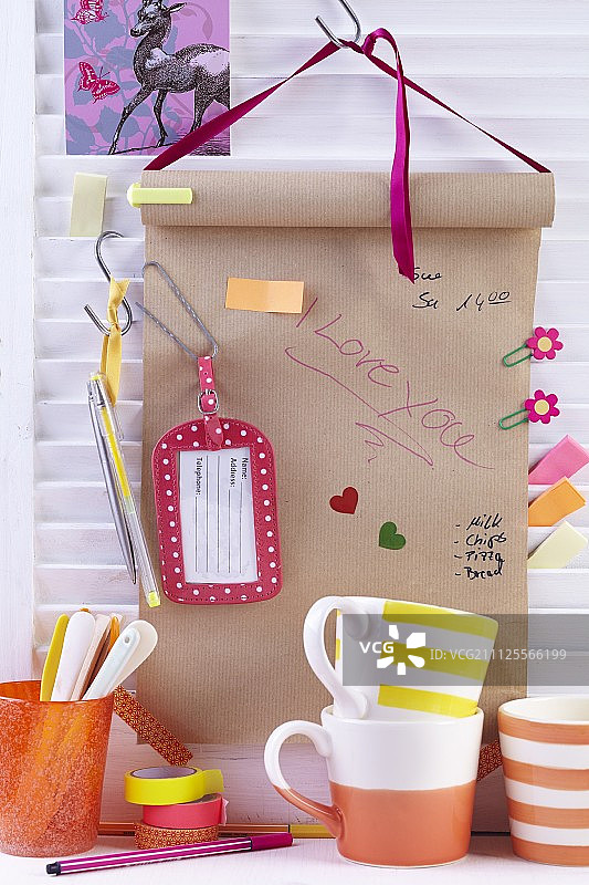 悬挂在架子上方的牛皮纸卷，用回形针、便利贴、标签和笔装饰图片素材