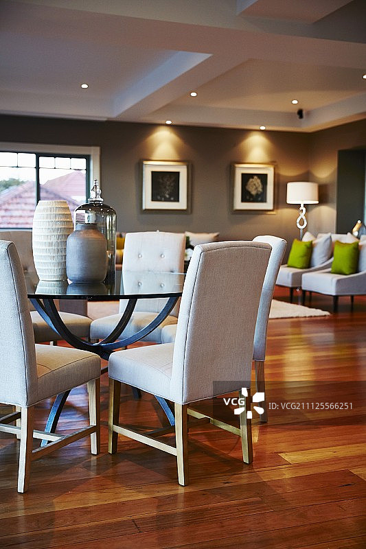 灰色房间角落里，圆形玻璃桌上的各种花瓶和白色软垫椅图片素材