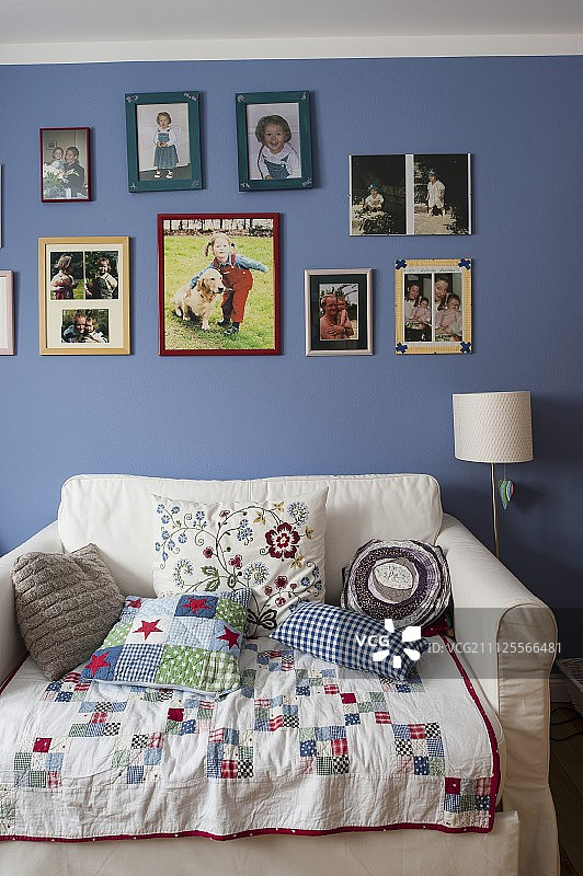 扶手椅床上方的拼布毯子和靠垫，蓝色墙壁上的图片图片素材