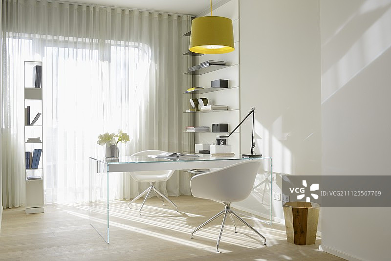 玻璃桌、白色设计师椅和阳光明媚的办公室里的通风储物架图片素材