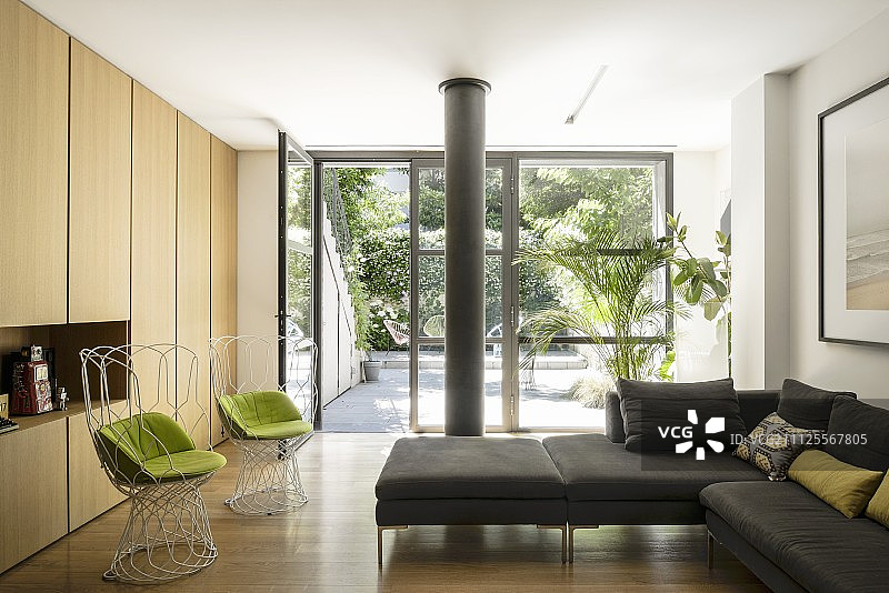 极简主义客厅，配现代金属丝椅、浅色木制橱柜和玻璃墙，可欣赏庭院景观图片素材