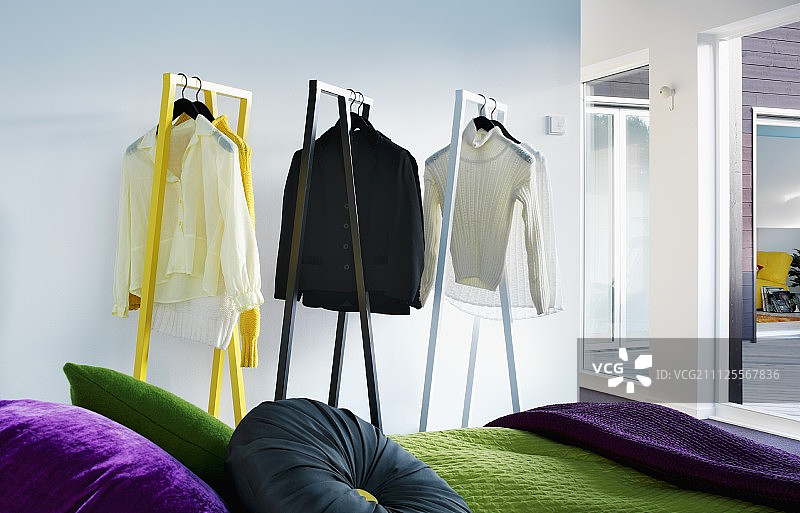 设计师服装架上的衬衫和套头衫，部分可见的床上有各种颜色的靠垫和绿色床罩图片素材