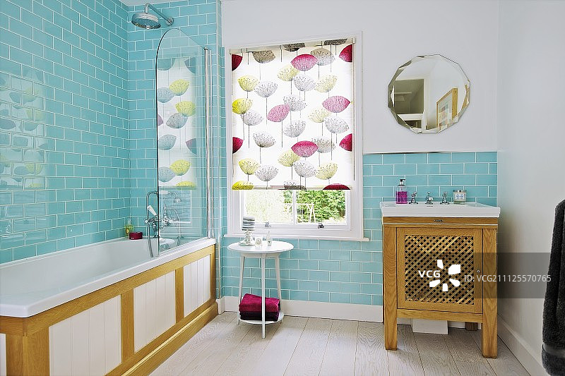 浴室配有淡蓝色墙砖、木质浴缸、带图案的卷帘窗和木制盥洗台上的水槽图片素材