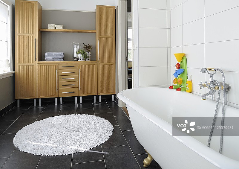 独立浴缸上的彩色浴缸玩具和复古龙头配件；背景是带集成搁板的橱柜图片素材