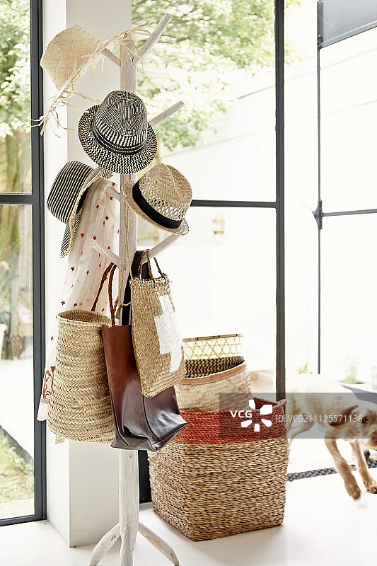 树状衣帽架上的帽子、堆叠的篮子和通往花园的开放式露台门图片素材