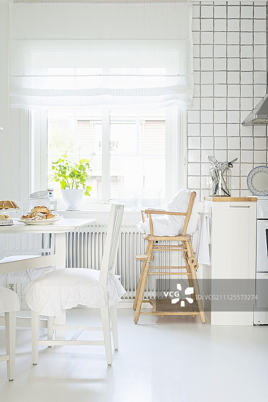 白色斯堪的纳维亚厨房的窗户下，用餐区配有褶皱坐垫和高脚椅图片素材