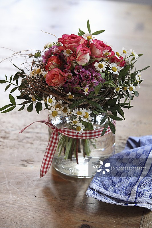 用格子带装饰的玻璃罐中的玫瑰和雏菊花束图片素材