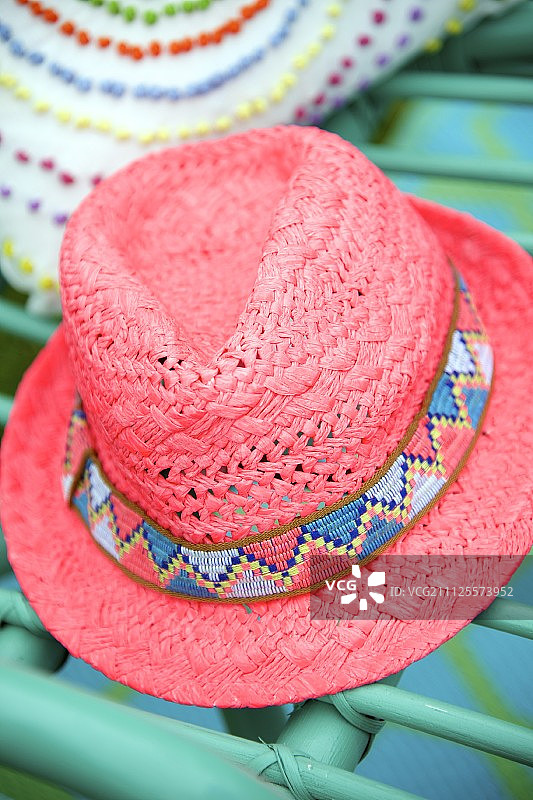 绿色柳条椅上带有花纹帽带的粉色草帽图片素材